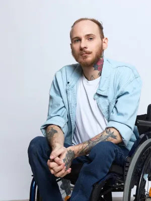 Man in a wheelchair wearing a light blue jacket and white shirt against a plain background