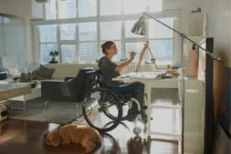 Person in a wheelchair working at a desk in a home office setting.